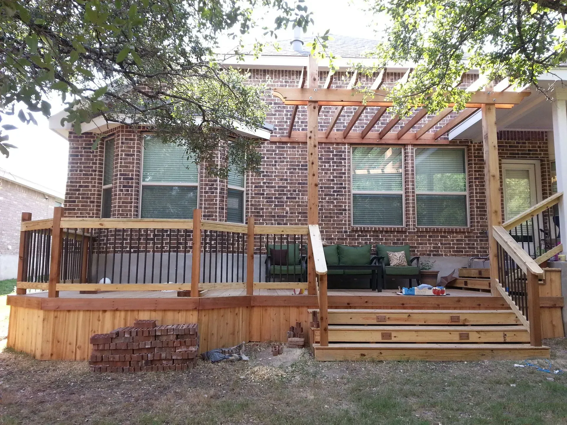 Backyard deck with pergola and brick house. Wooden deck with steps and railing.