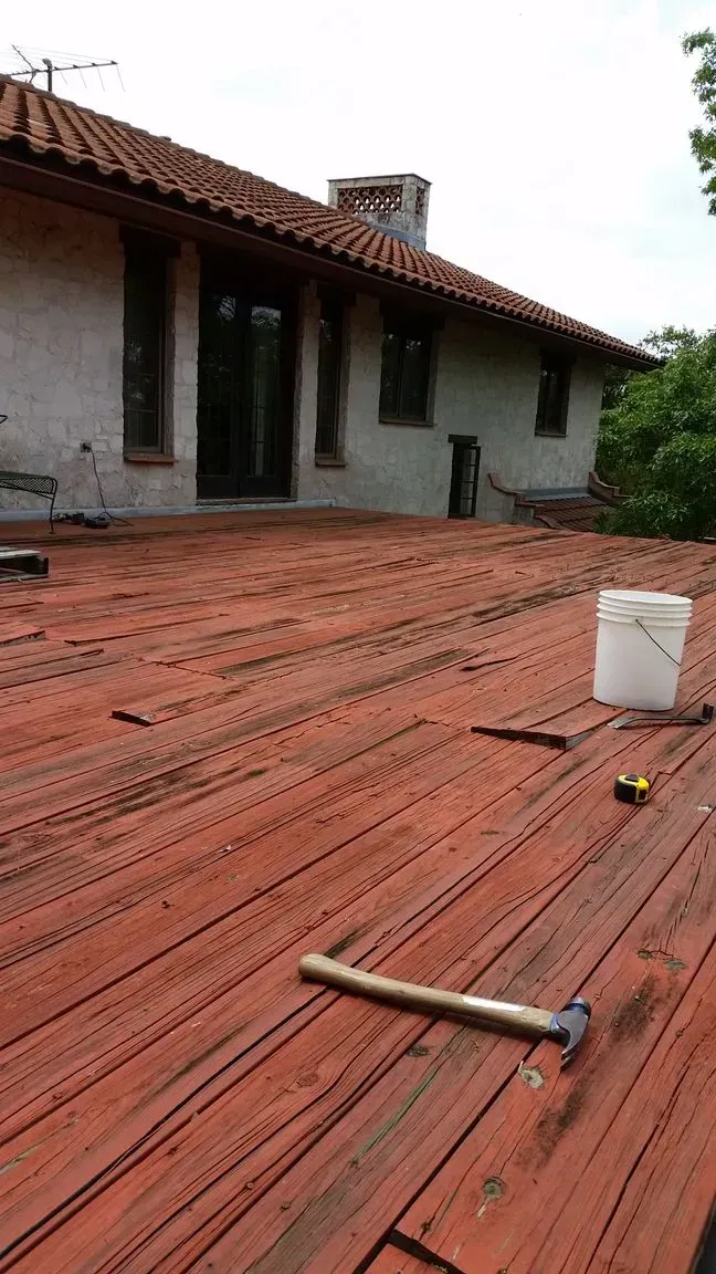 Red tile roof with tools and a bucket, house in background.