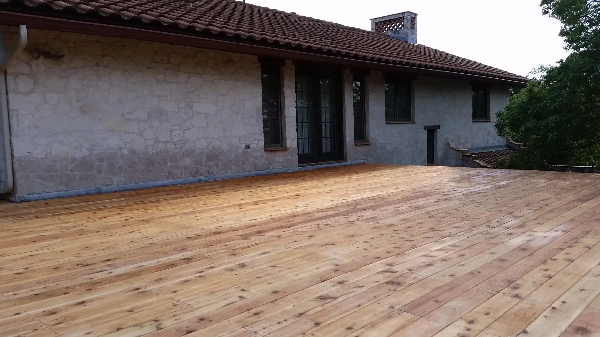 Wooden deck extending from a stucco house with a tiled roof.