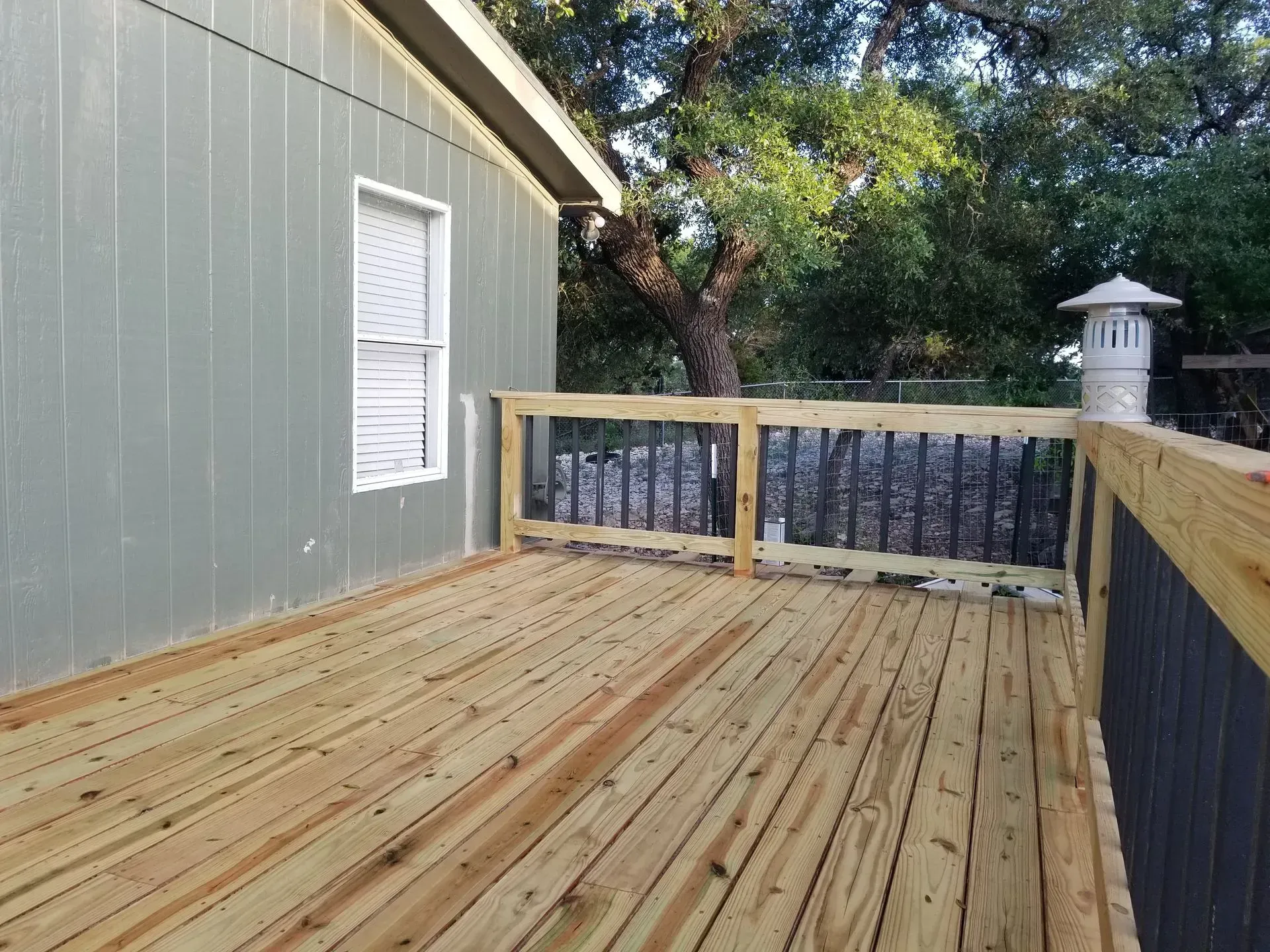Wooden deck with railing attached to a light green house. A window is visible.