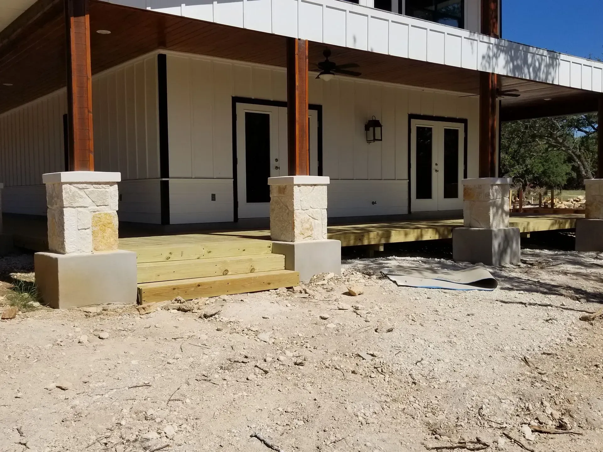 A white building with a wooden deck and stone pillars under a covered porch.