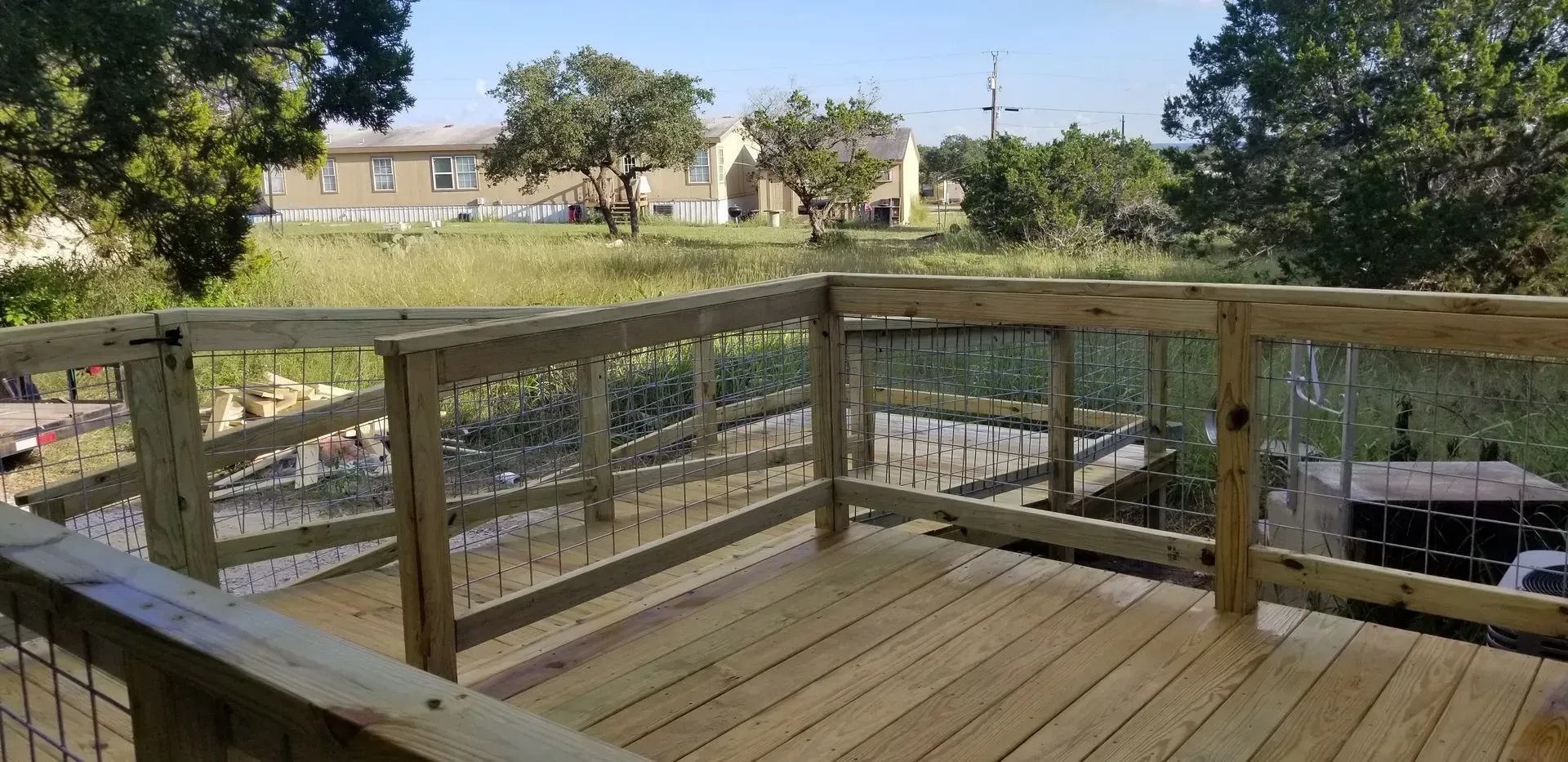 Wooden deck overlooking a grassy area with trees and buildings in the distance, sunny day.