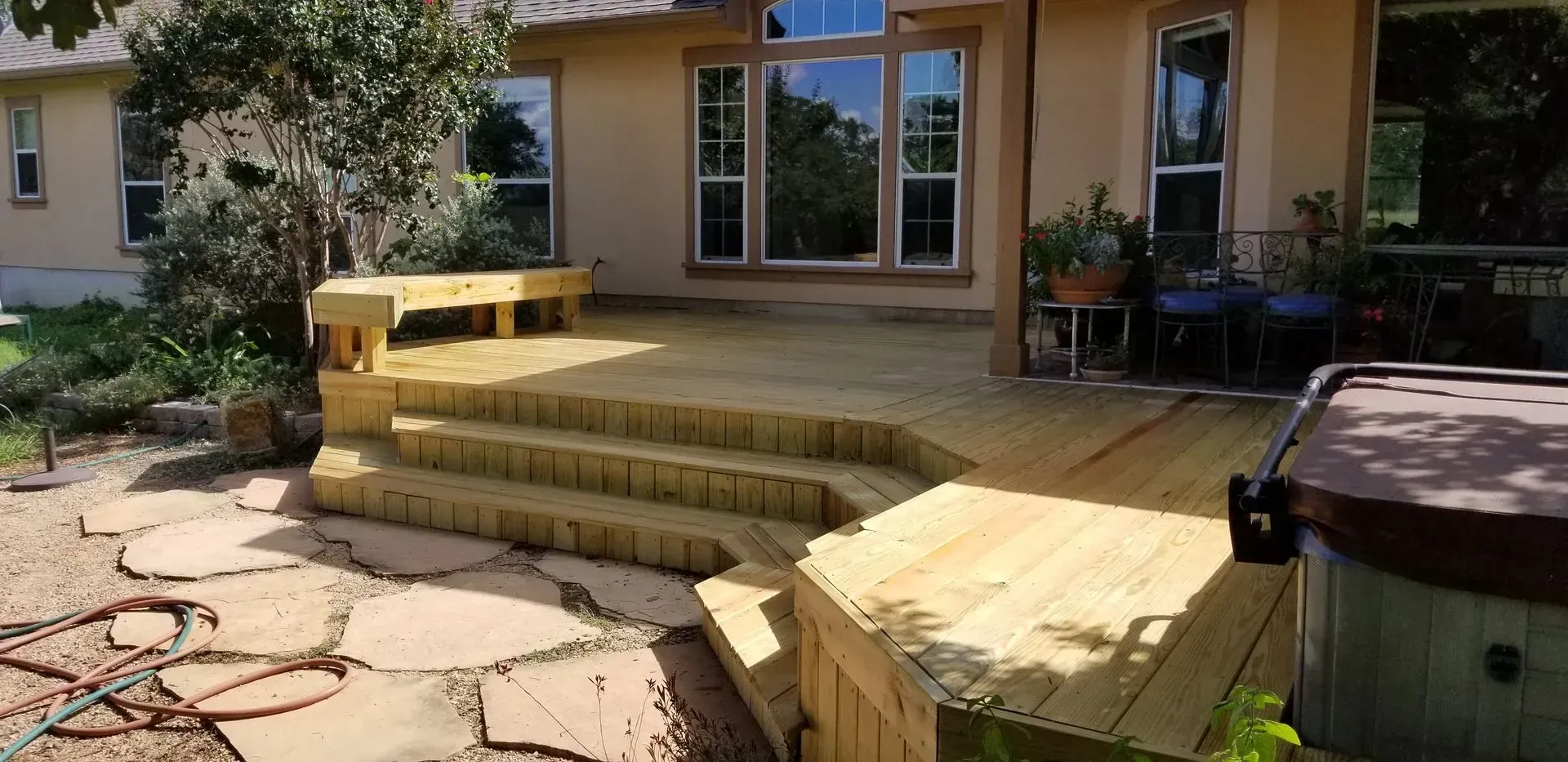 Wooden deck with steps, bench, and hot tub. House in background.