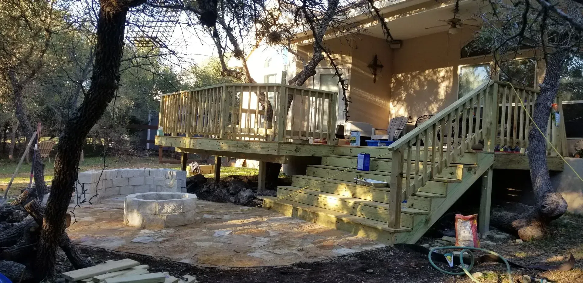 Wooden deck with stairs, a stone fire pit, and a house in a wooded area.