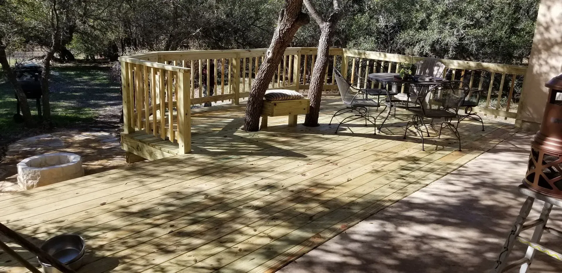 Wooden deck with railing, seating, and trees in a sunny outdoor setting.