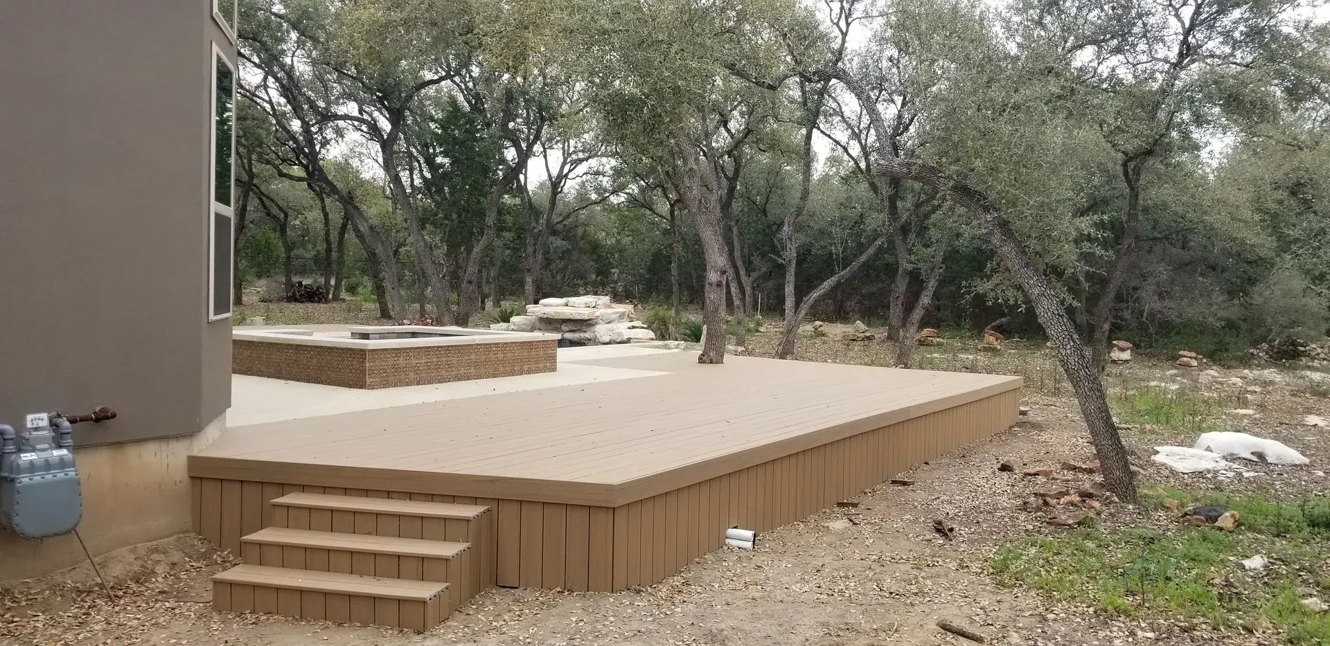Outdoor deck with stairs, a fire pit, and trees in a natural setting.