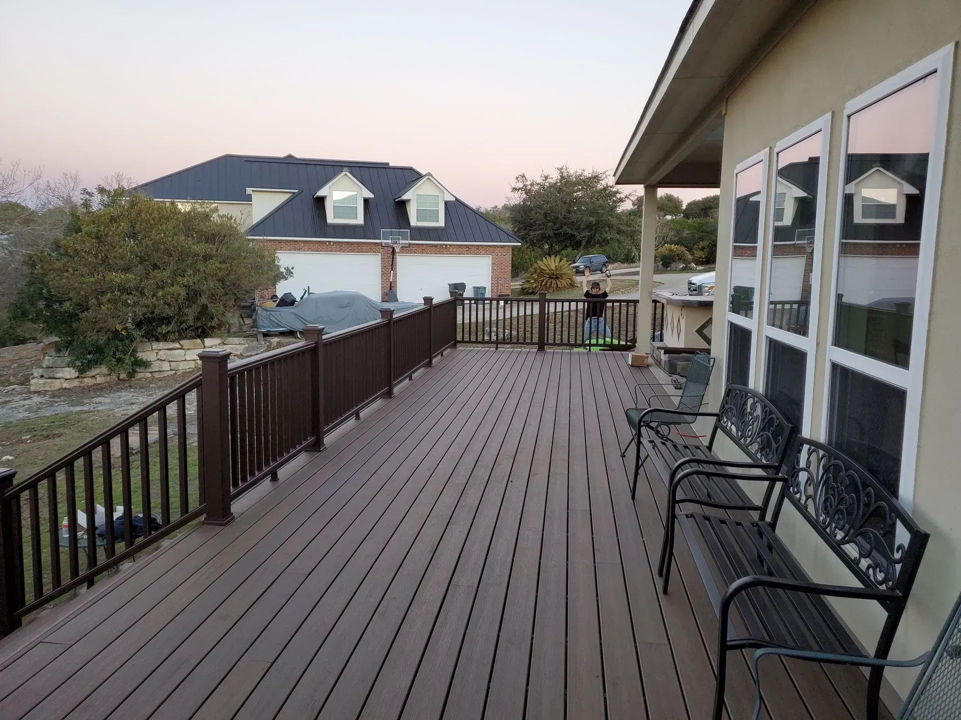 Wooden deck with brown railing, benches, and house in background.