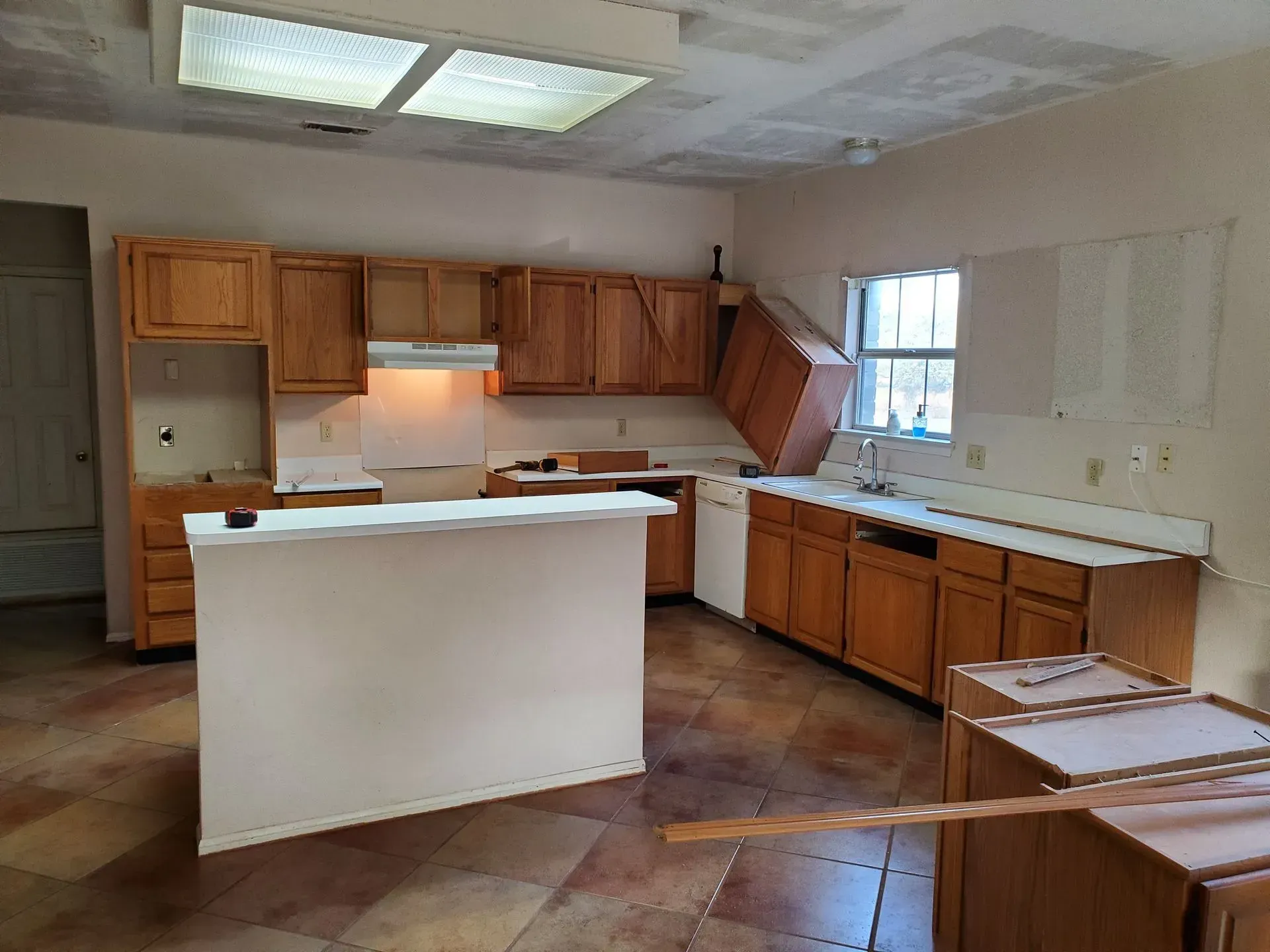 Kitchen with wood cabinets, island, and tile floor, under construction, with a window and a bright ceiling light.