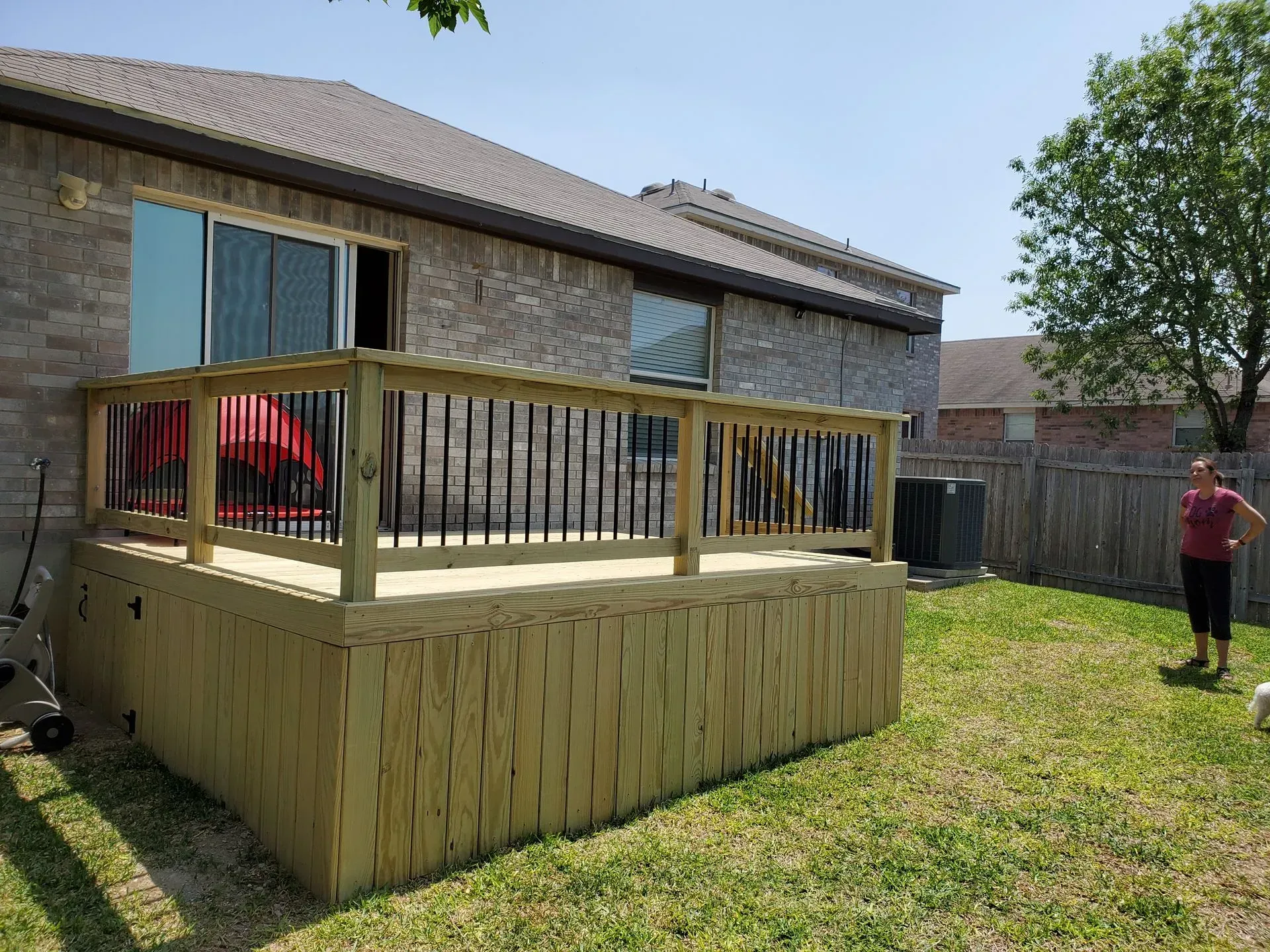 Newly built wooden deck attached to a brick house, person standing in the grass nearby.