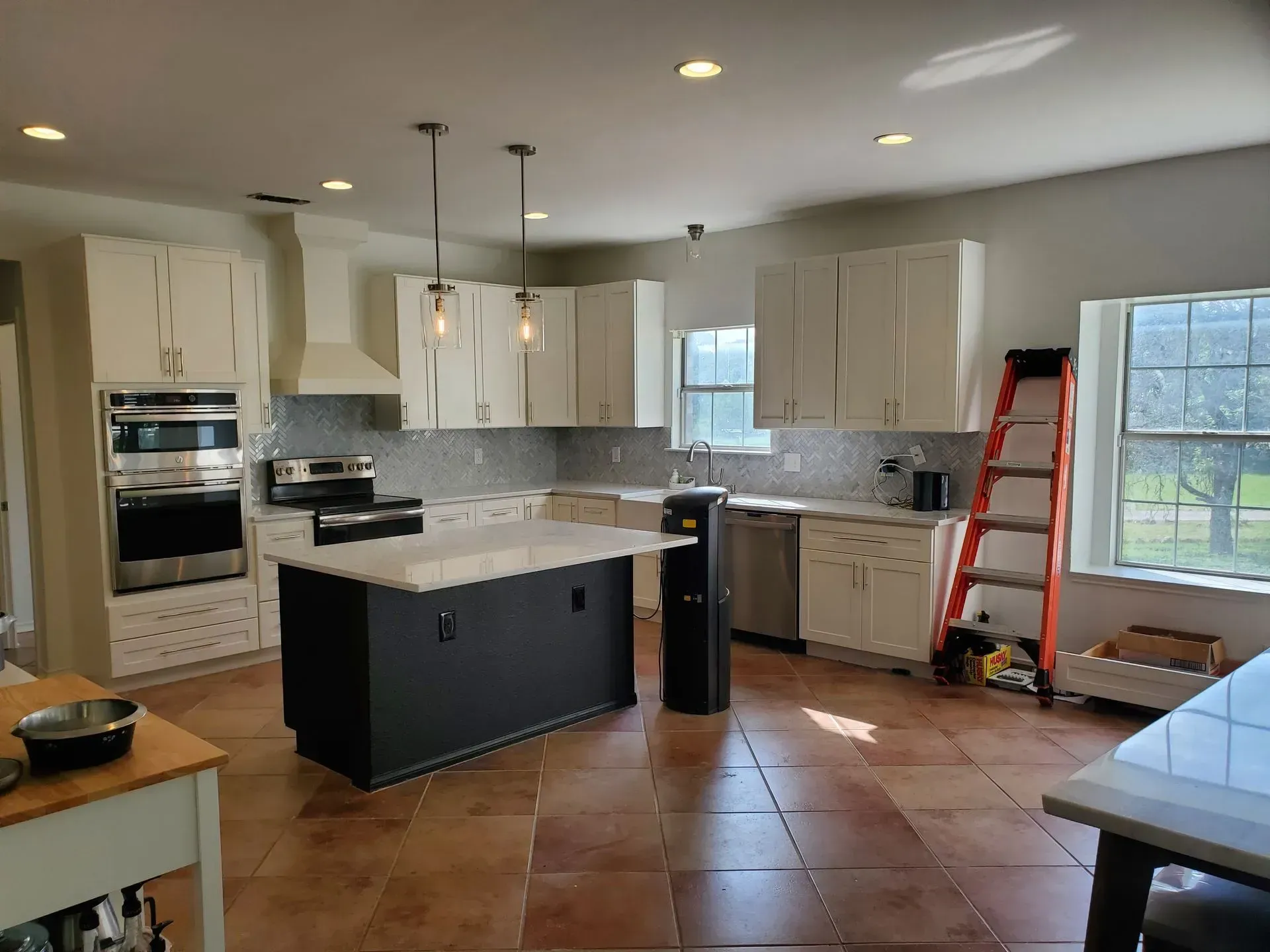 Renovated kitchen with white cabinets, black island, stainless steel appliances, and terra-cotta tile floor.