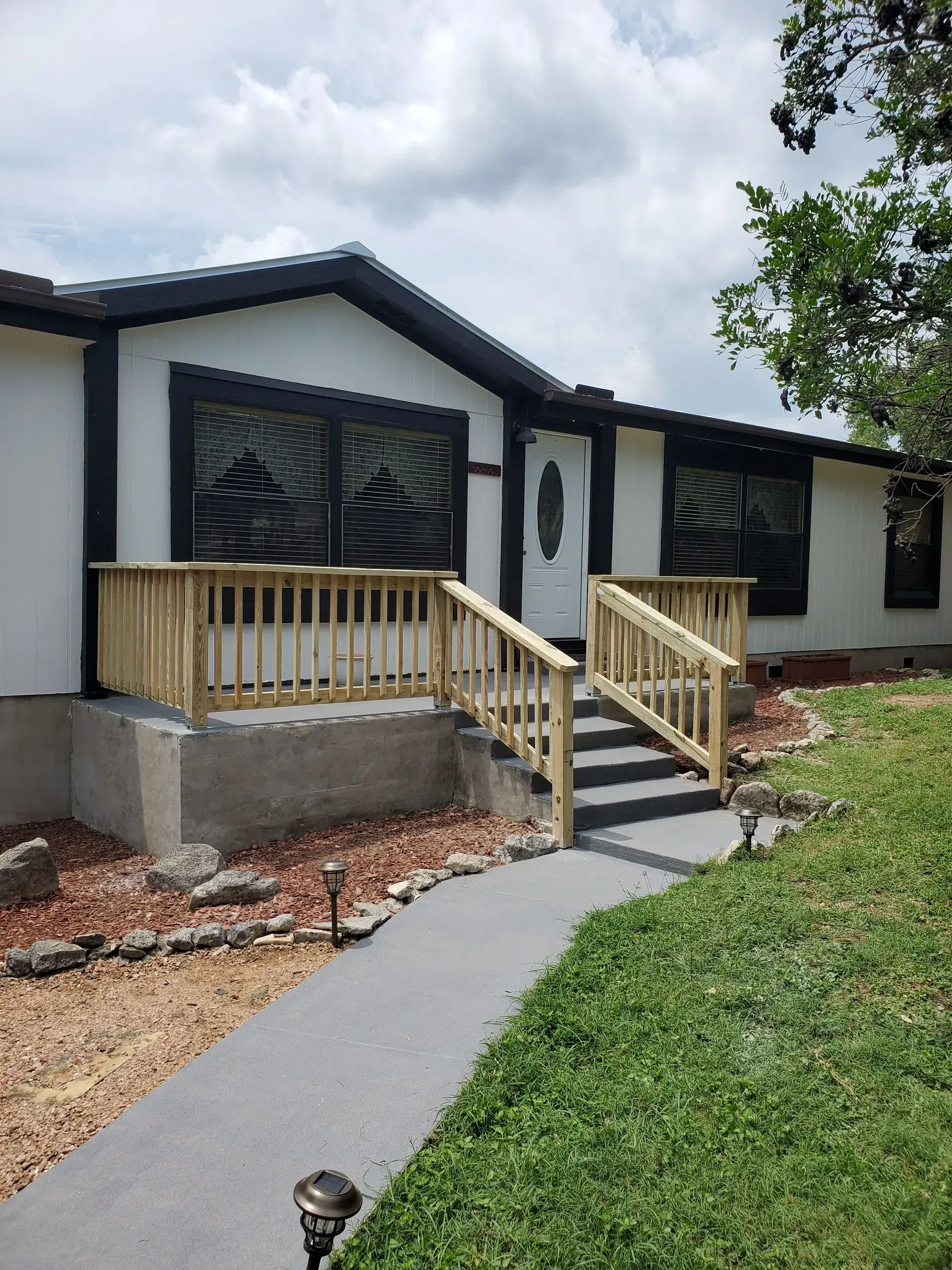 Exterior of a house with a concrete walkway, wooden deck, and landscaping.