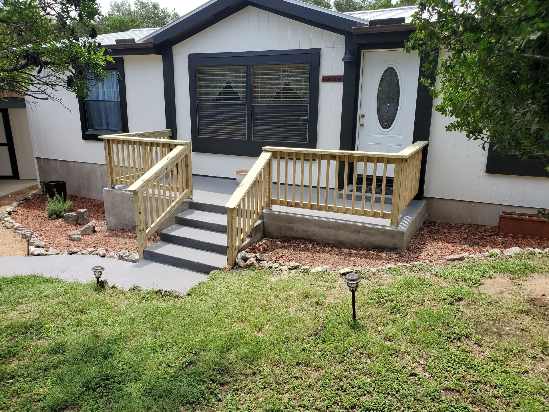 A house with a front porch, stairs, and landscaping. The house is white with black trim.