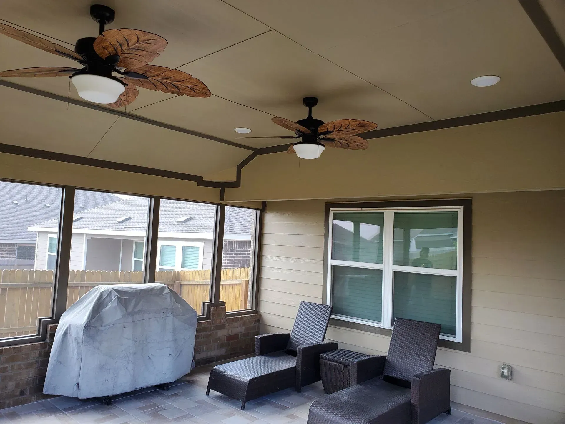 Covered patio with two ceiling fans, lounge chairs, and a grill.
