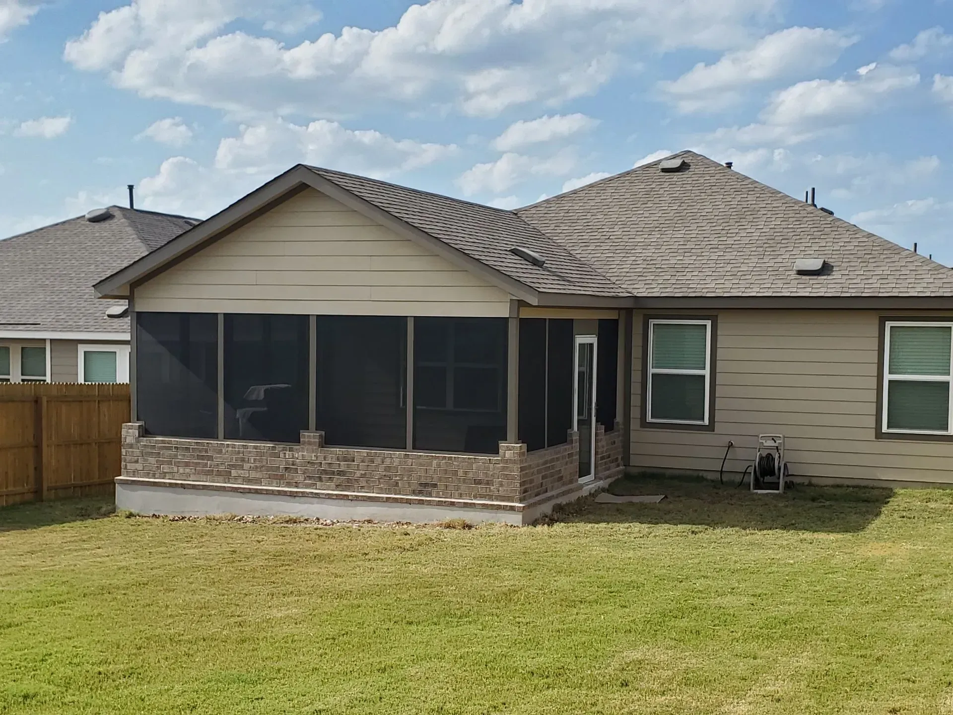 Backyard view of a house with a screened-in porch and tan siding under a blue sky.