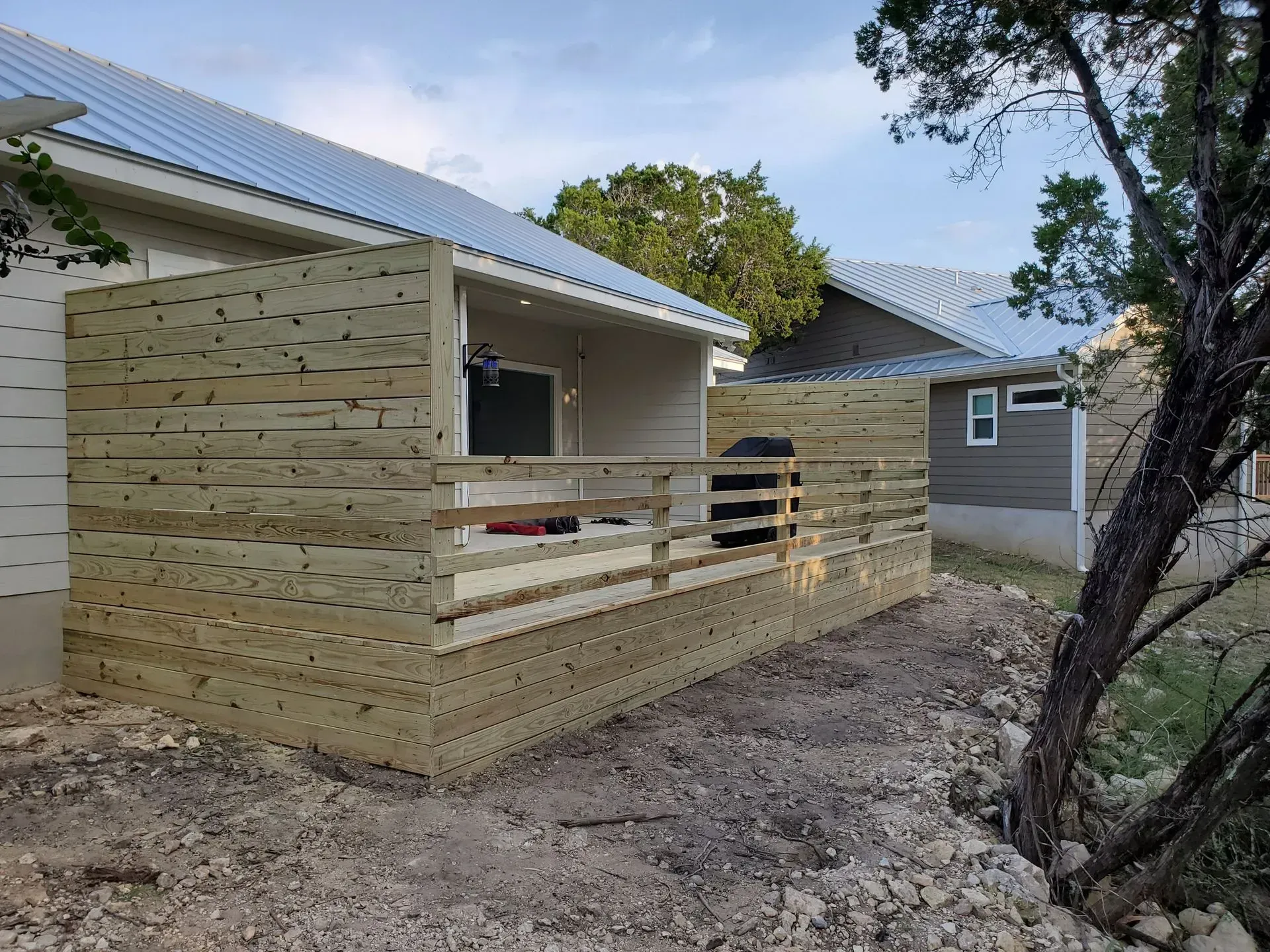 Wooden deck and fence attached to a house with a gray roof, in an outdoor setting.