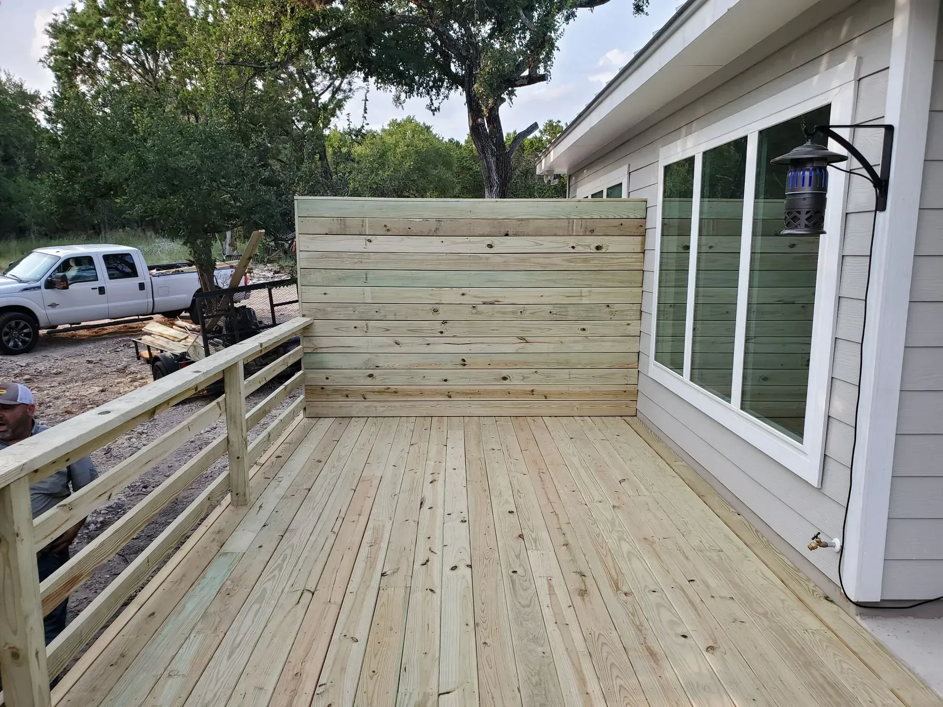 Wooden deck with horizontal privacy fence next to a building with large windows. A white truck is visible.