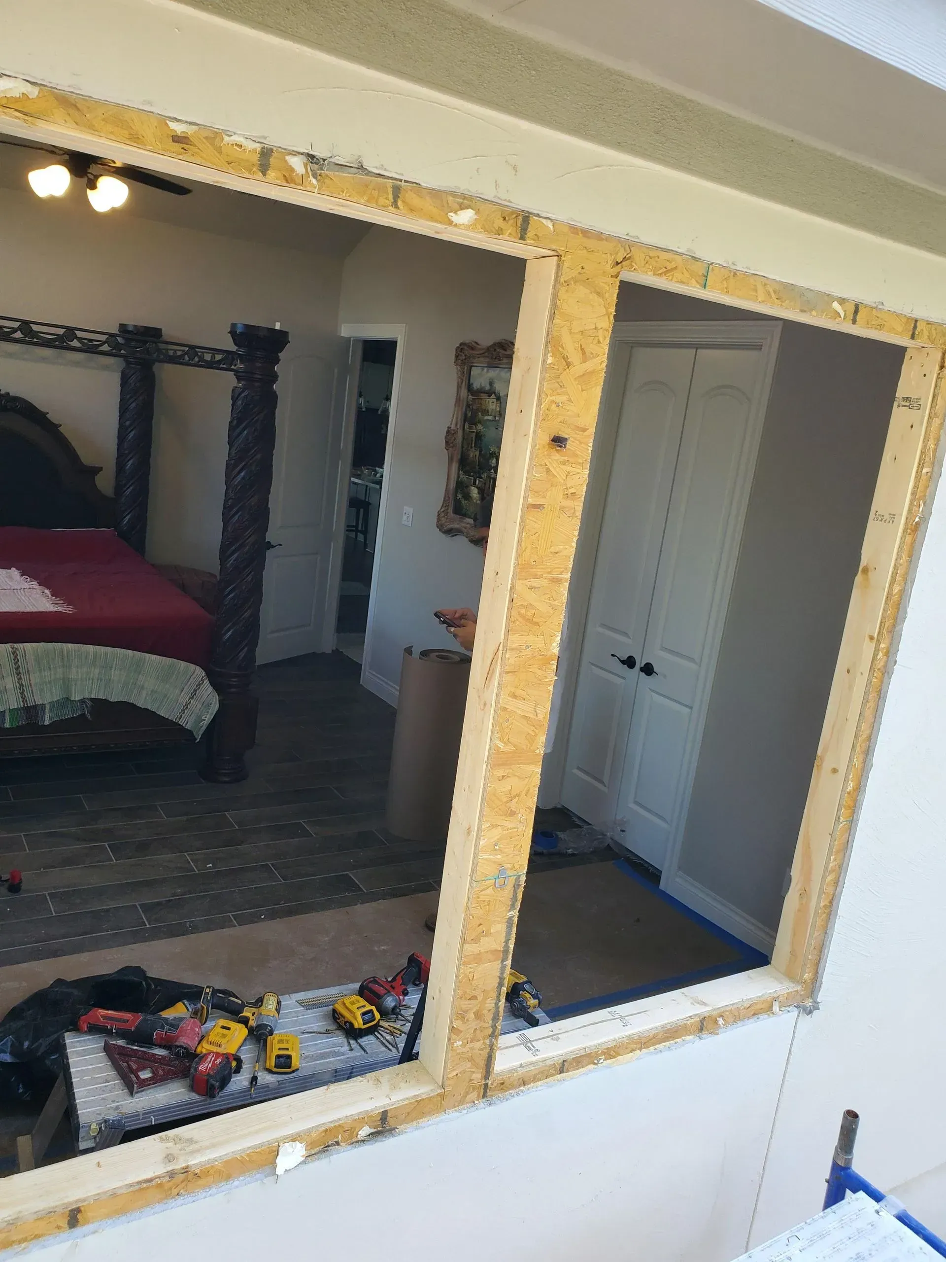 Window frame during renovation, revealing a bedroom interior with bed and closet.