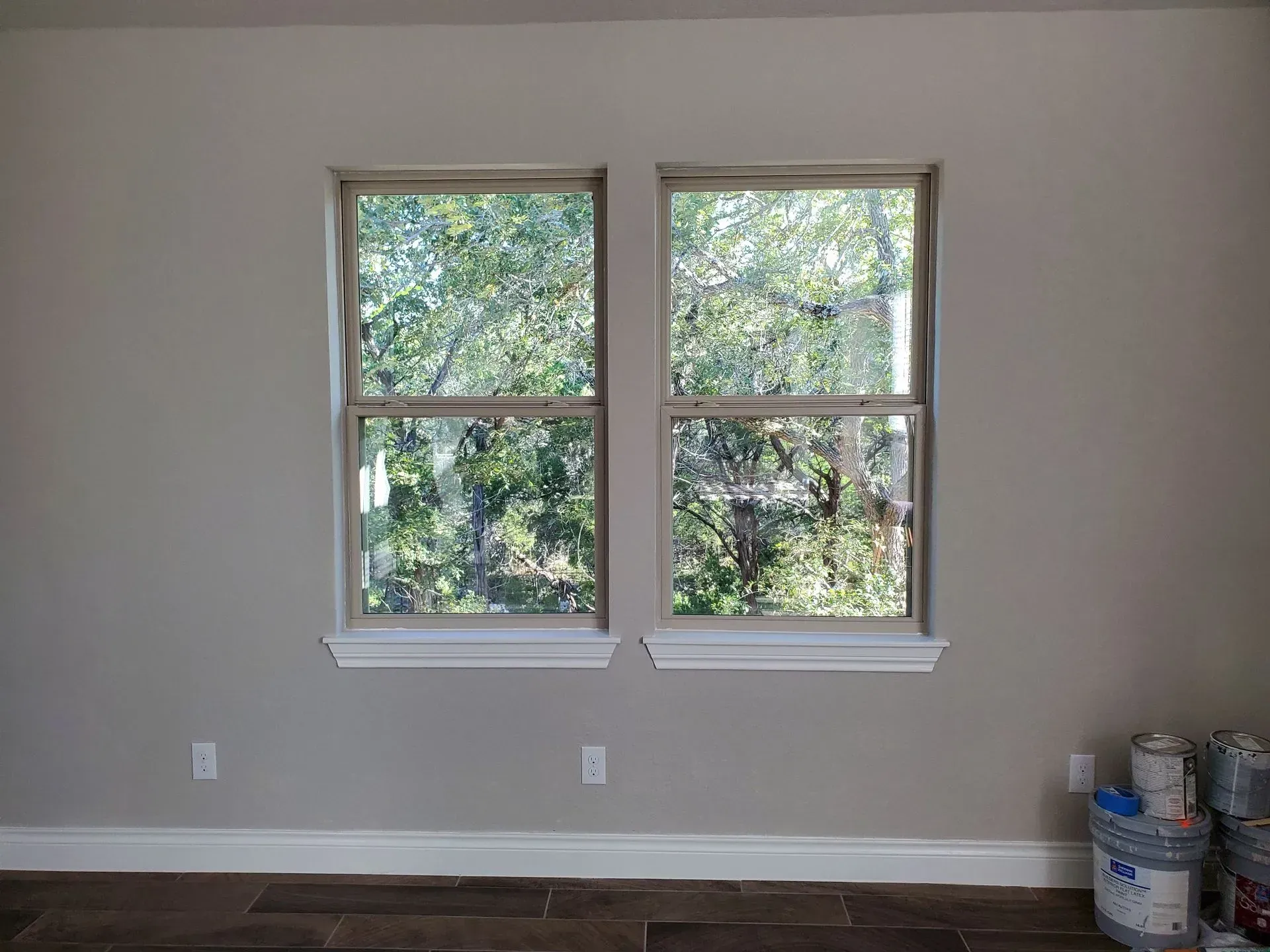 Two vertical windows centered on a gray wall with white trim. Green trees are visible through the windows.