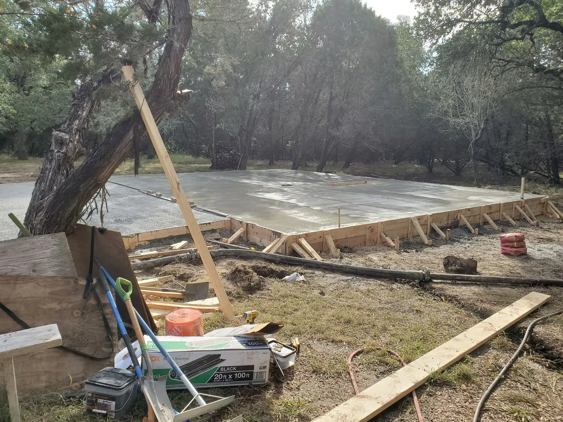 Concrete slab poured within wooden forms, surrounded by tools and construction materials.