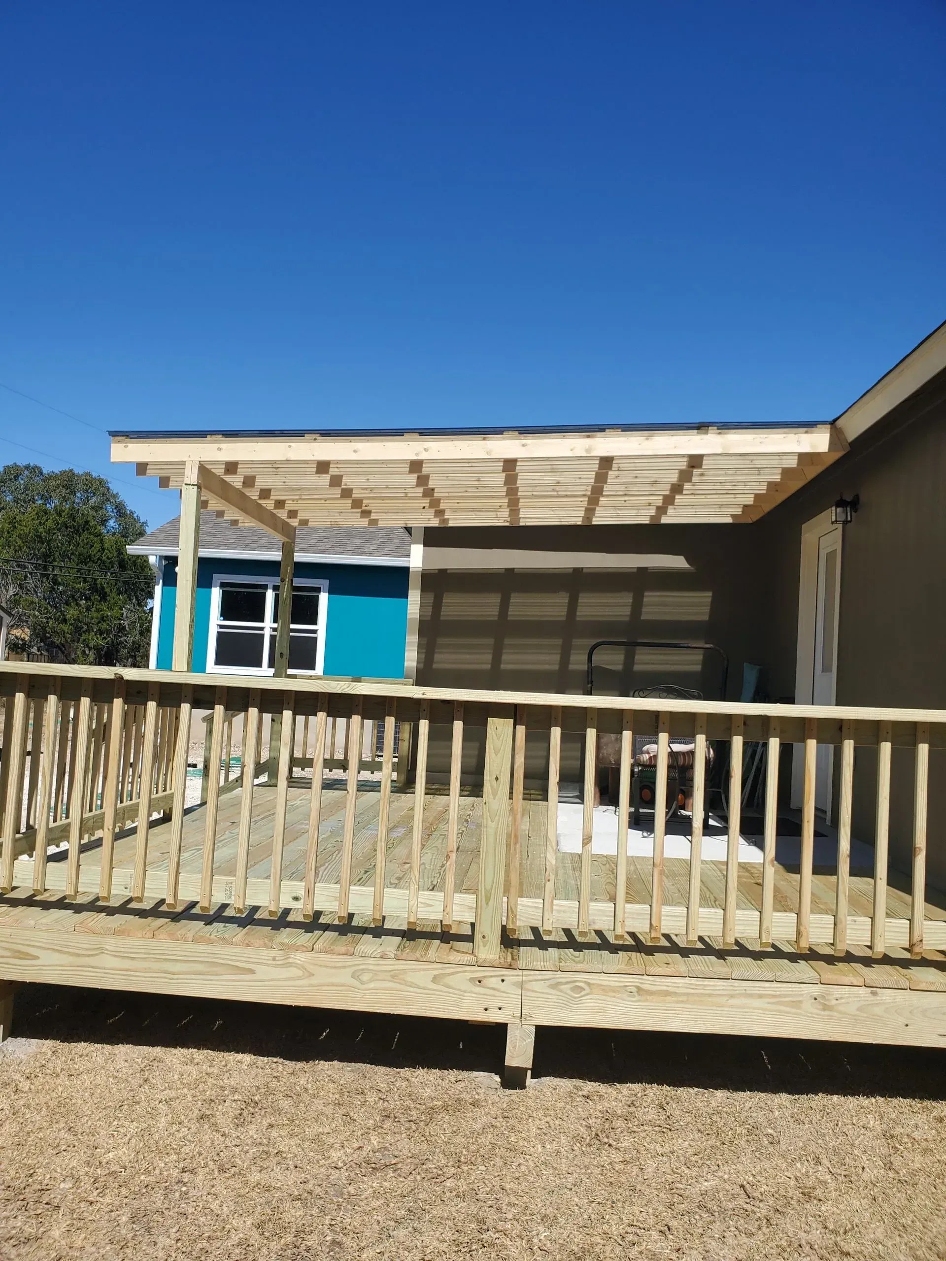 Wooden deck with pergola attached to a tan building. Turquoise building in the background.