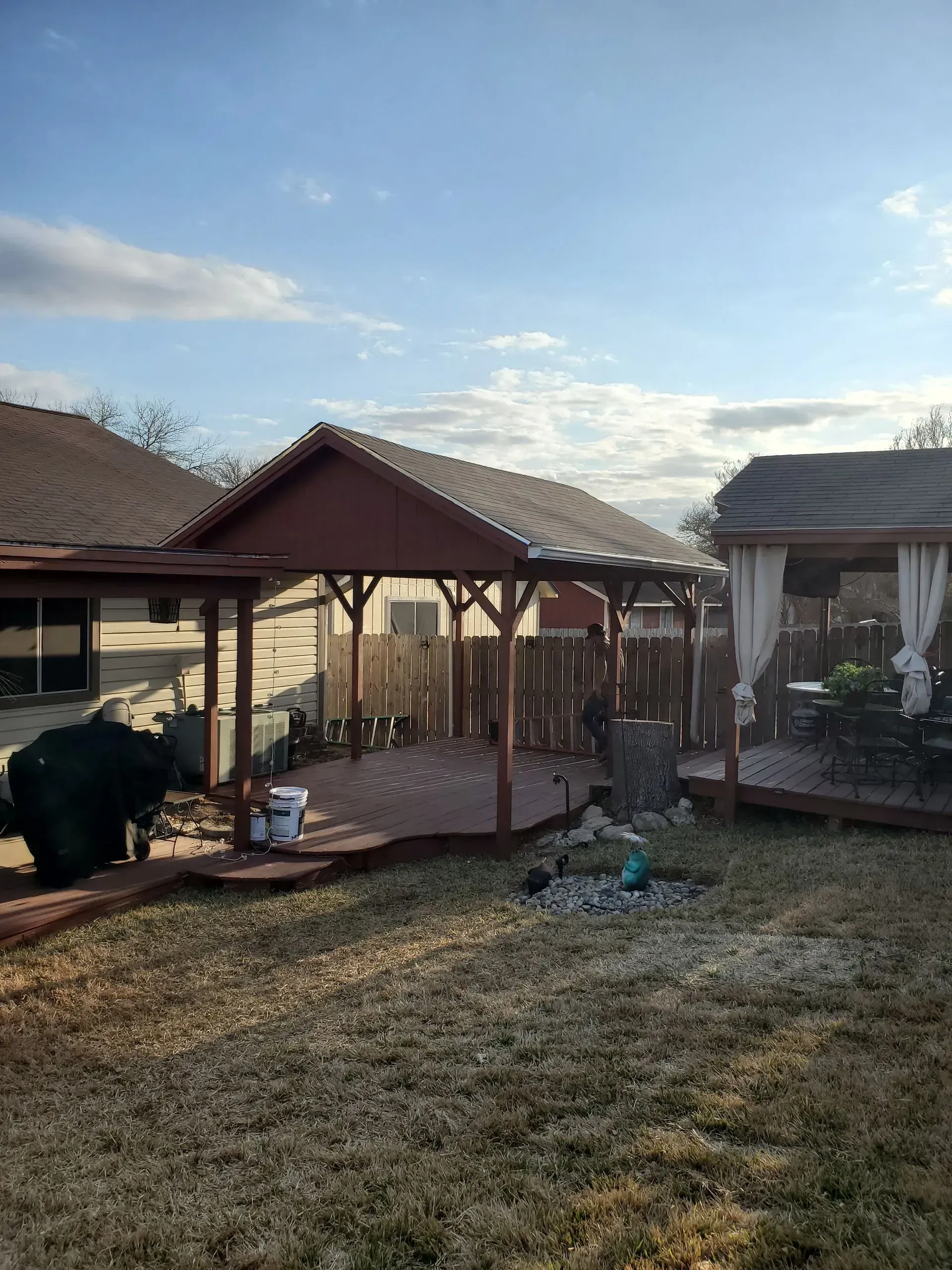 Backyard with a brown wooden deck, two covered structures, and a brown fence.