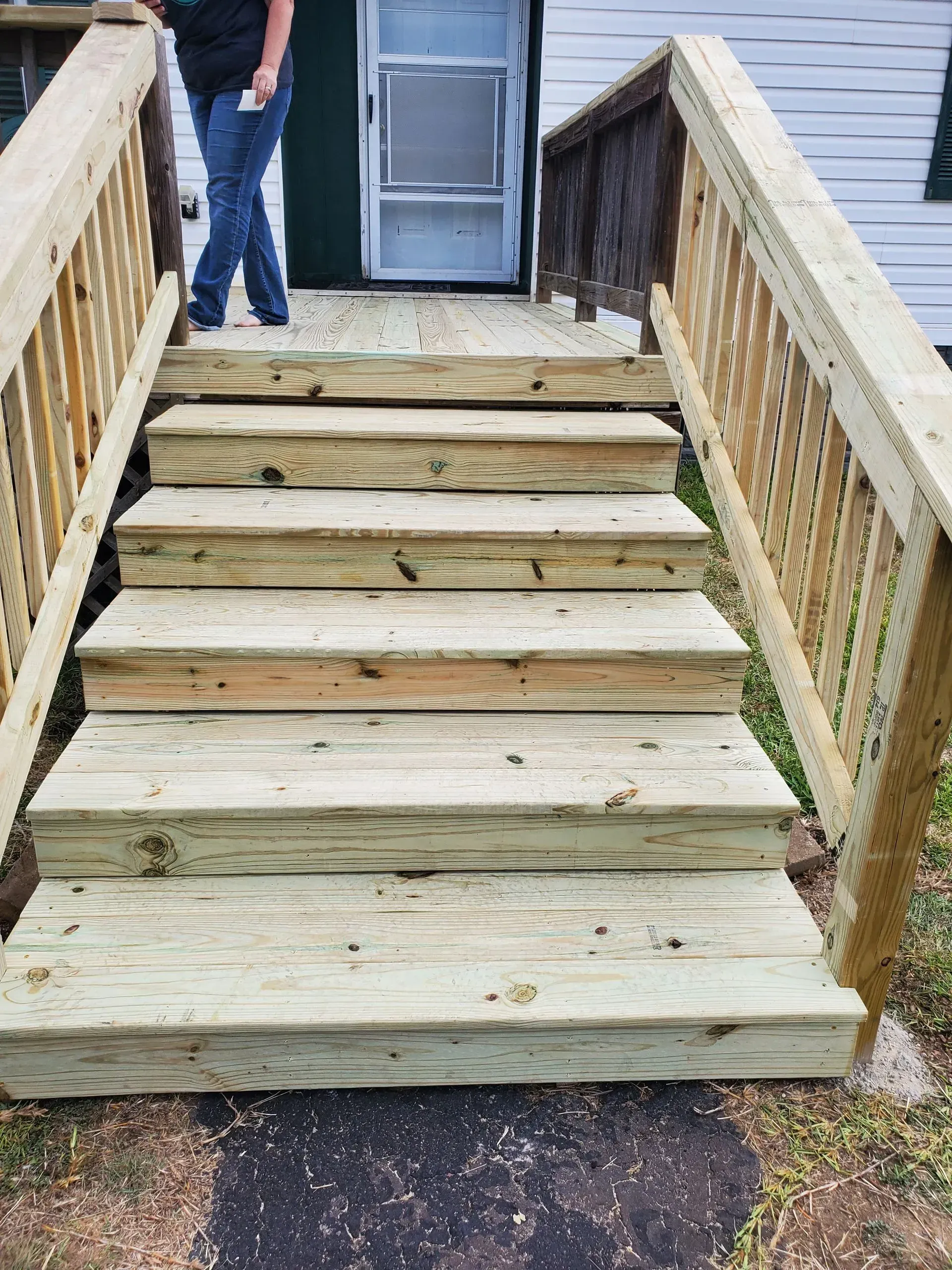 Wooden outdoor stairs leading to a door; person in jeans standing near the door.