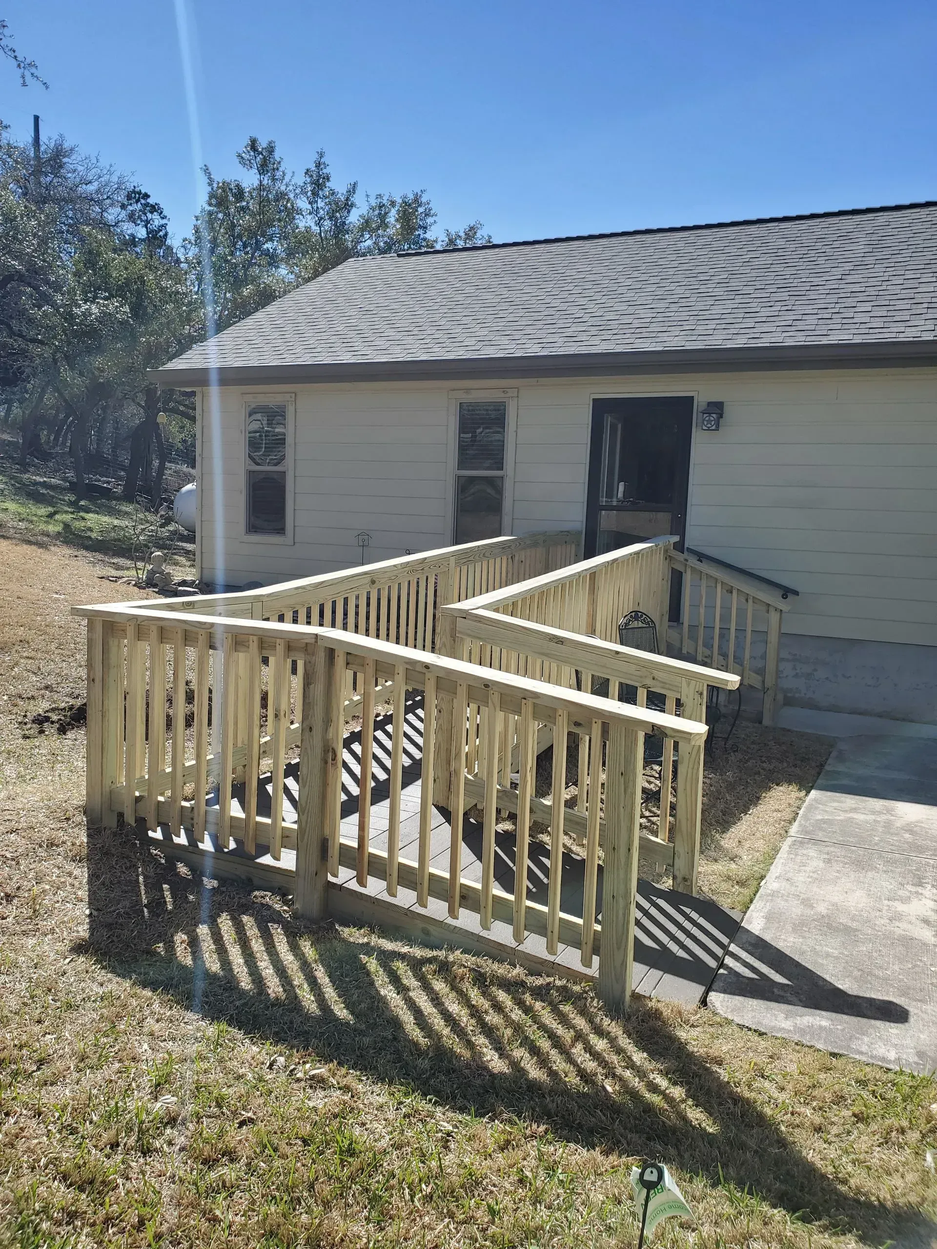 Ramped entry to a light-colored building with a dark roof. Wooden railing and walkway. Bright, sunny day.