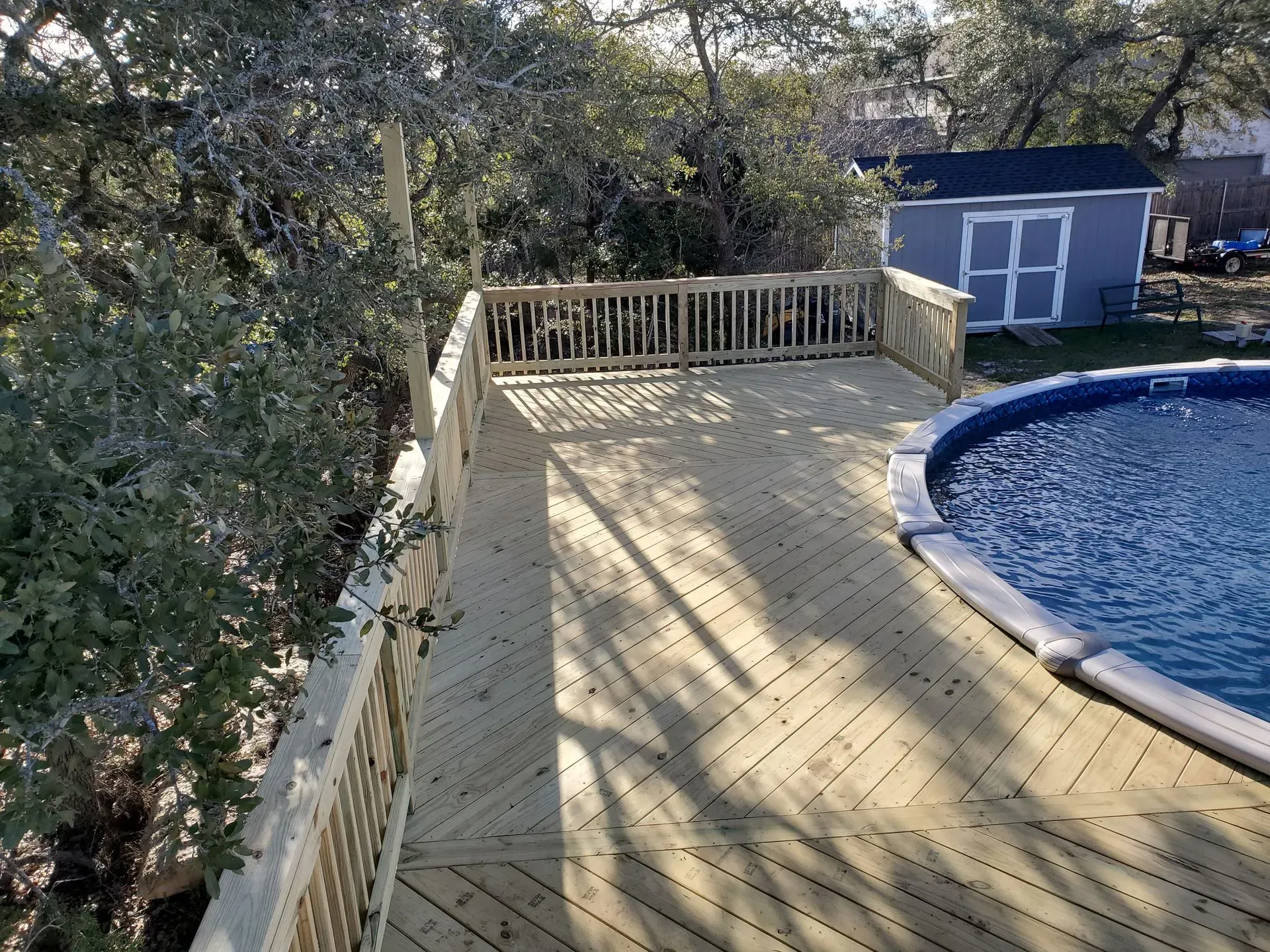 Wooden deck surrounding an above-ground pool; blue shed in the background.