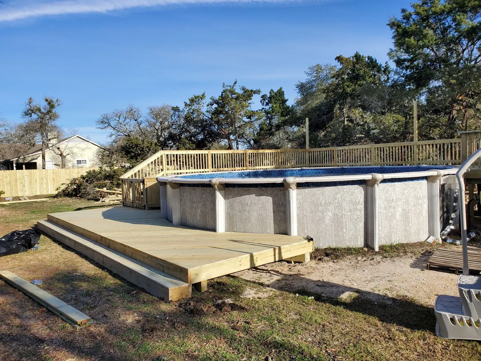 Above-ground pool with wooden deck and railing in a backyard setting on a sunny day.