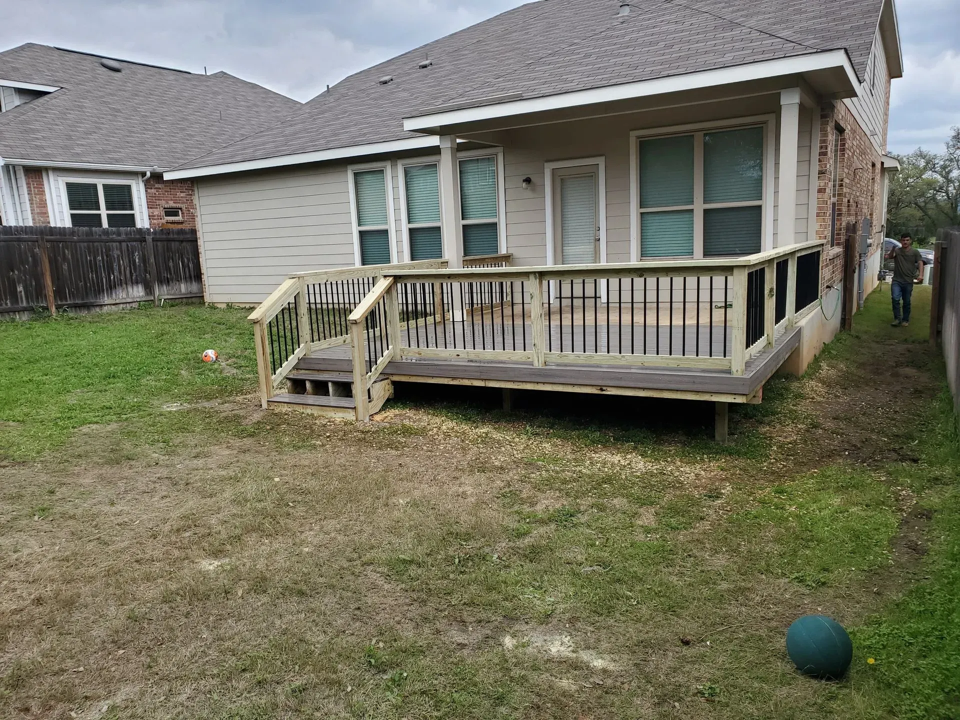Wooden deck attached to a two-story beige house with a grassy backyard.