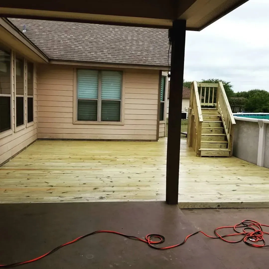 Backyard deck with wooden stairs to a pool, under a house overhang.