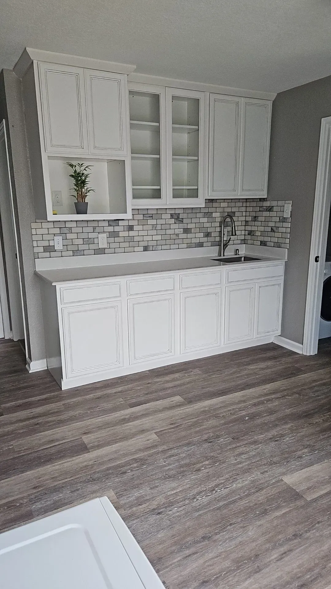 White kitchen cabinets, mosaic backsplash, gray walls, and wooden floor.