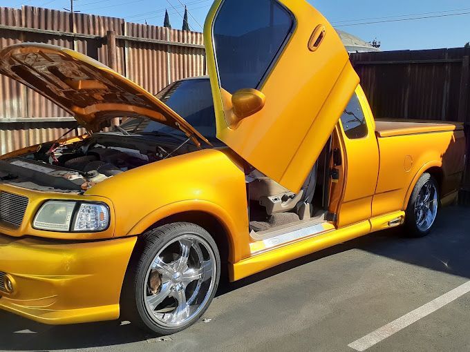 A yellow truck with the hood up is parked in a parking lot