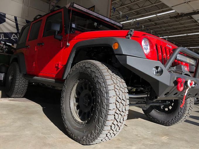 A red jeep with a black bumper is parked in a garage.