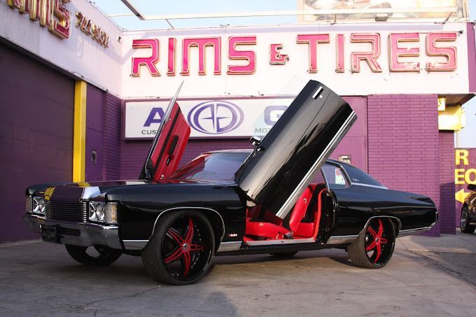 A black car is parked in front of a store called rims & tires