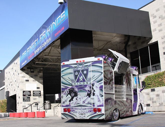A purple and white food truck is parked in front of a building