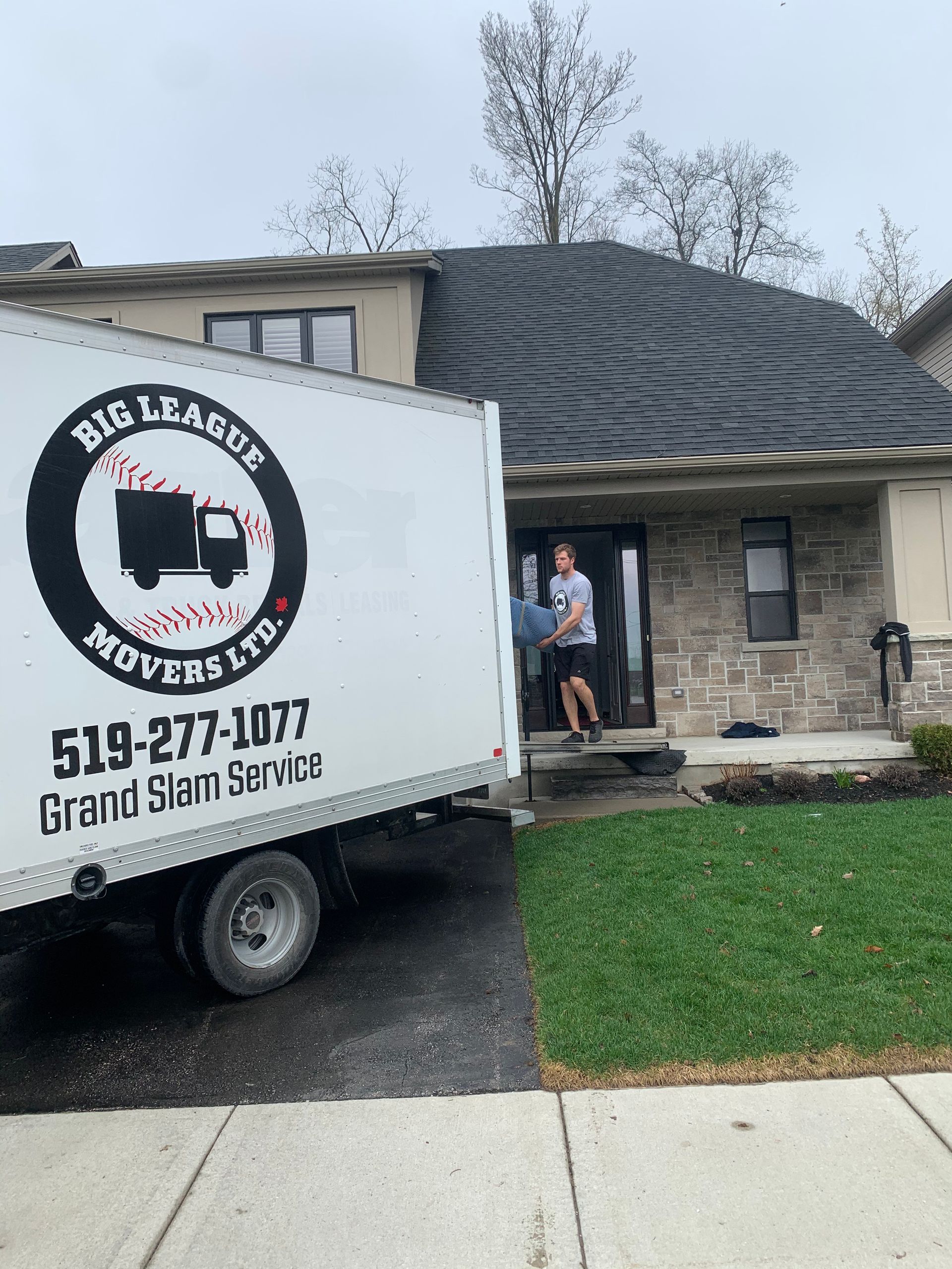 A big league movers truck is parked in front of a house.