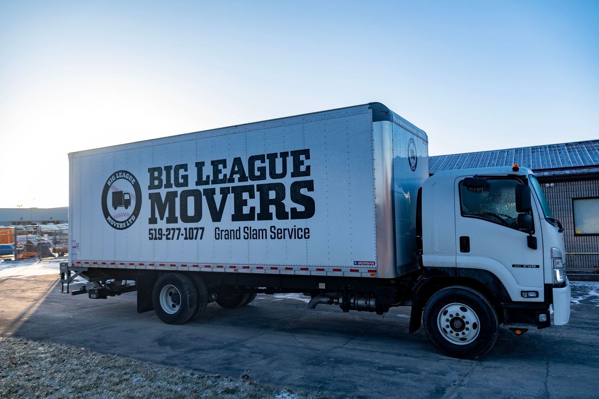 A big league movers truck is parked in front of a building.