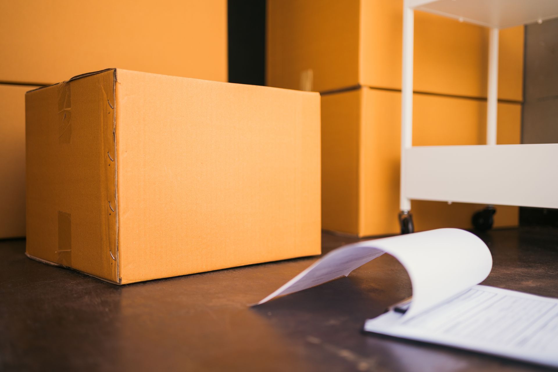 Cardboard boxes stacked in a room; a notepad is on the floor in front of a box.