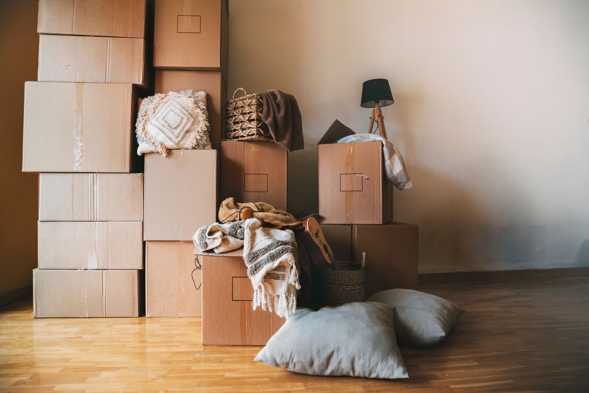 Moving boxes stacked in a room, pillows, blankets, and a lamp sit nearby, suggesting a recent move.
