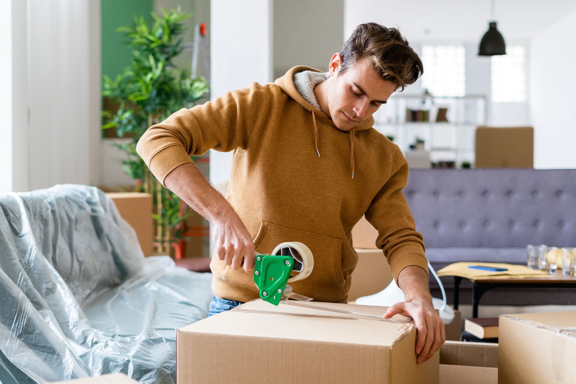 A man is taping a cardboard box in a living room.