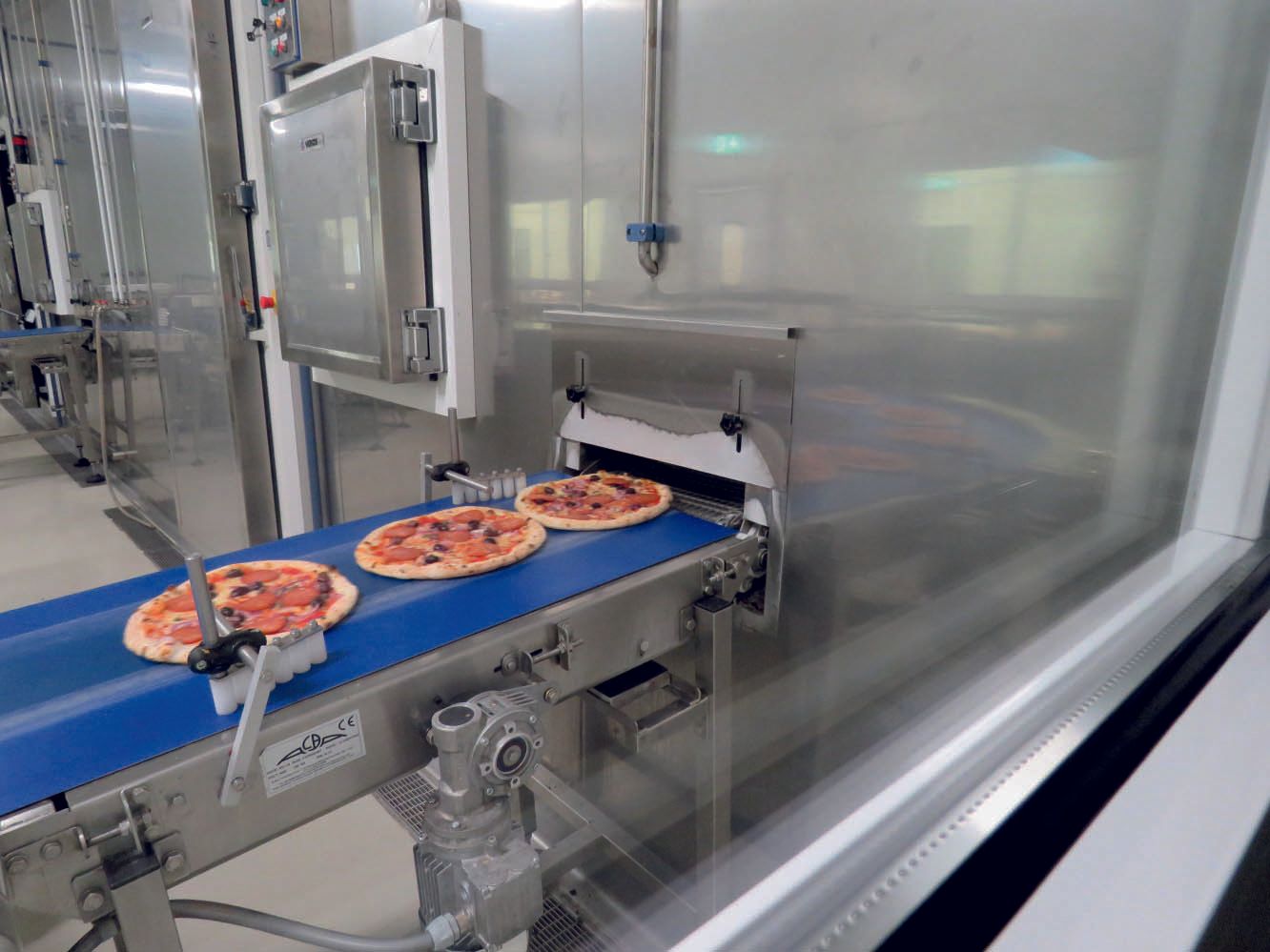Frozen pizzas on the conveyor belt of a temperature reduction unit