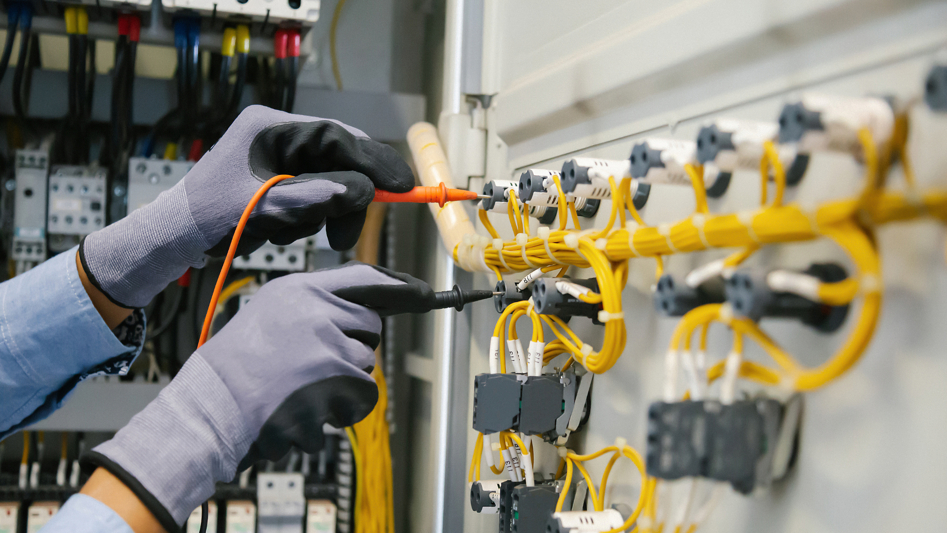 An electrician is working on an electrical panel with a screwdriver.