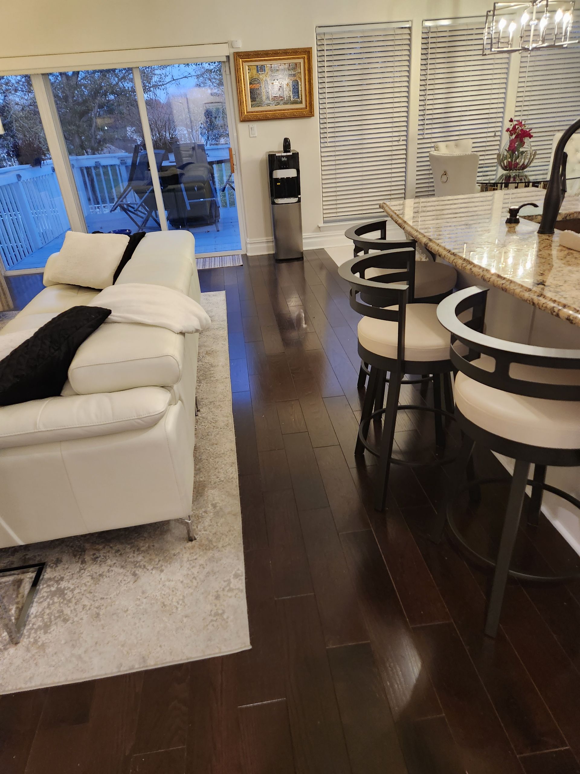 Living room with white couch, dark wood floors, kitchen island with stools, and large windows overlooking a snowy deck.