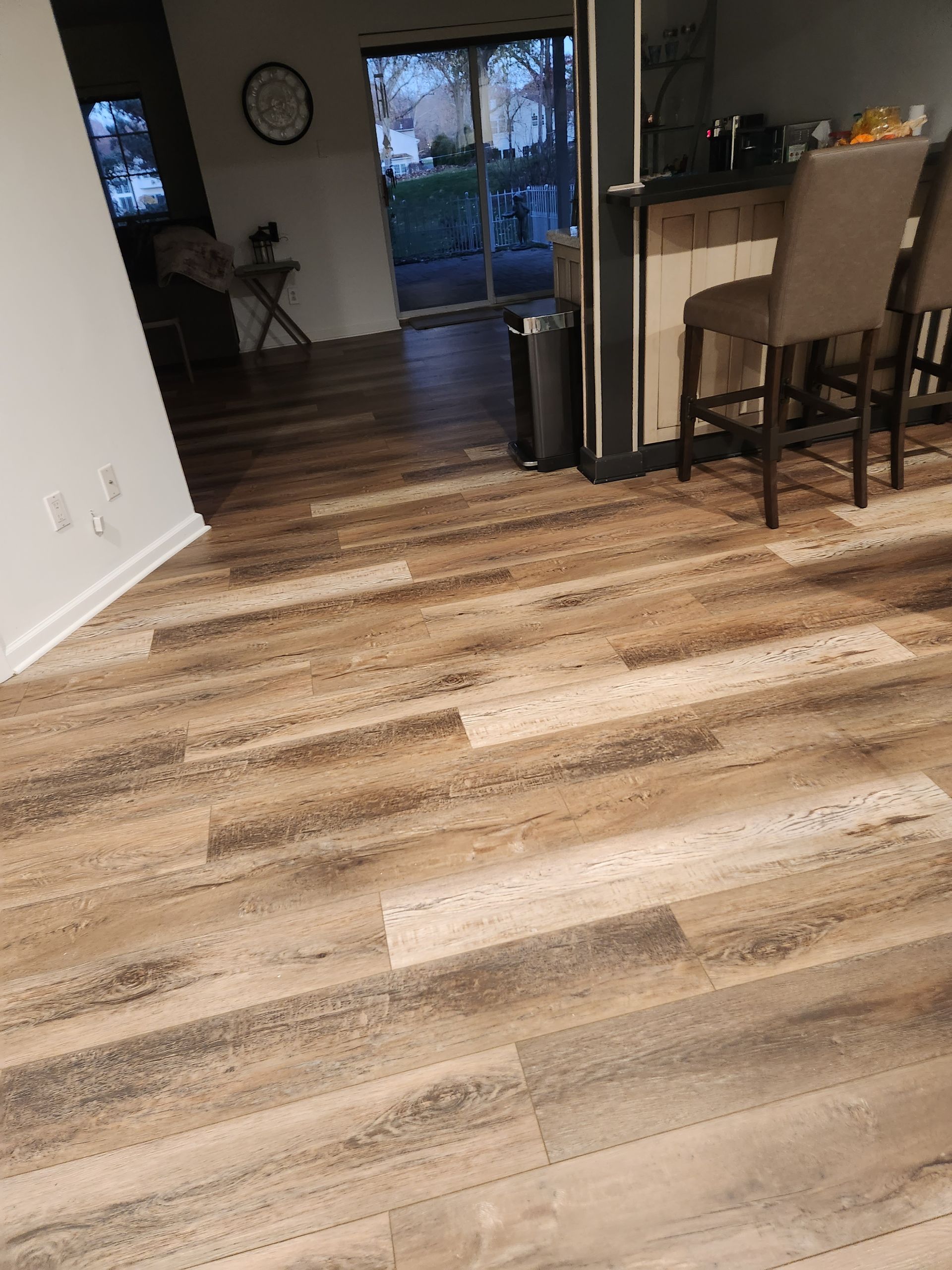 Wooden floor in a home, with a view of the outside and kitchen bar with stools.