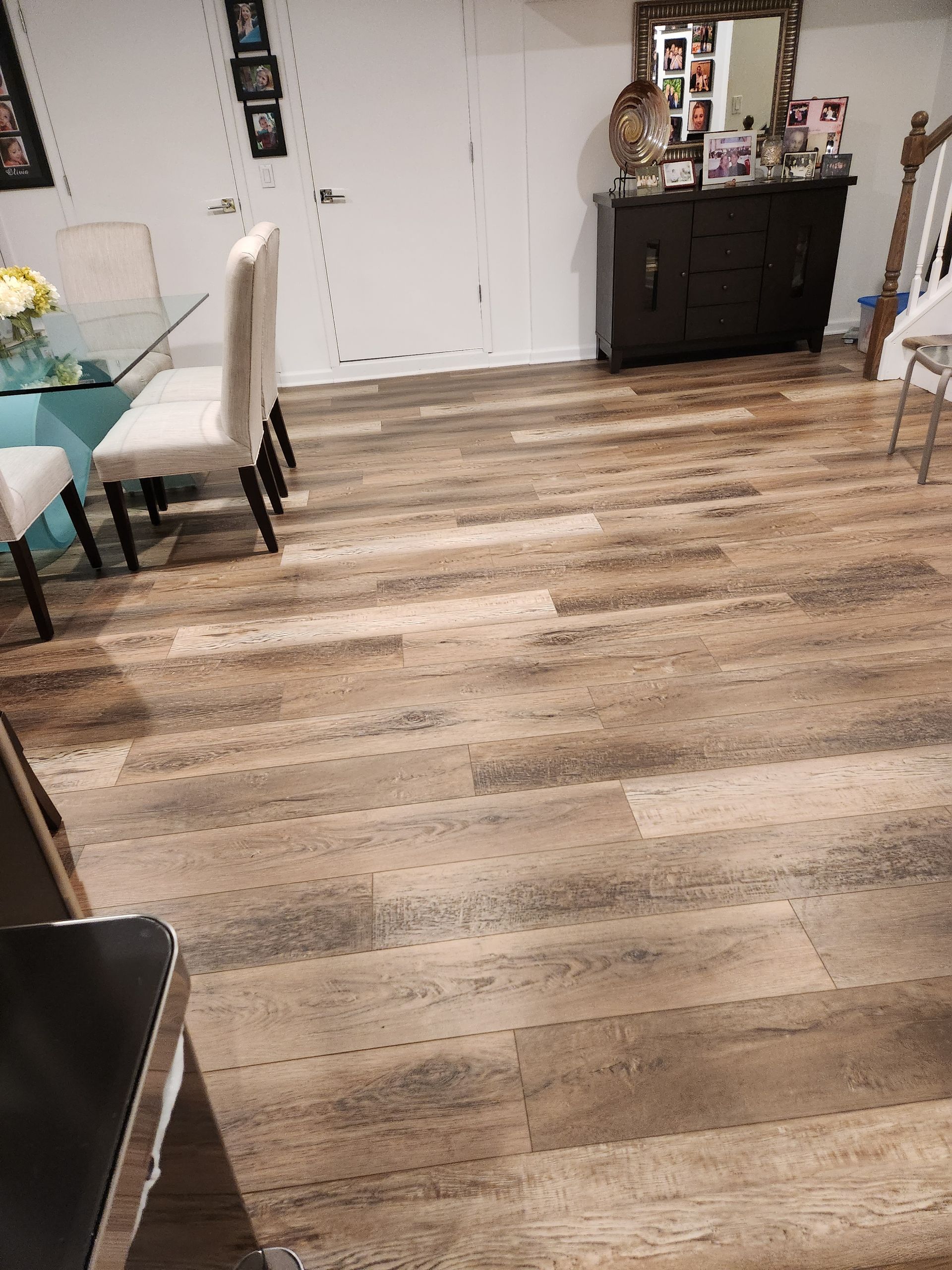 Wooden floor in a room with a dining table, chairs, a buffet, and a white door.