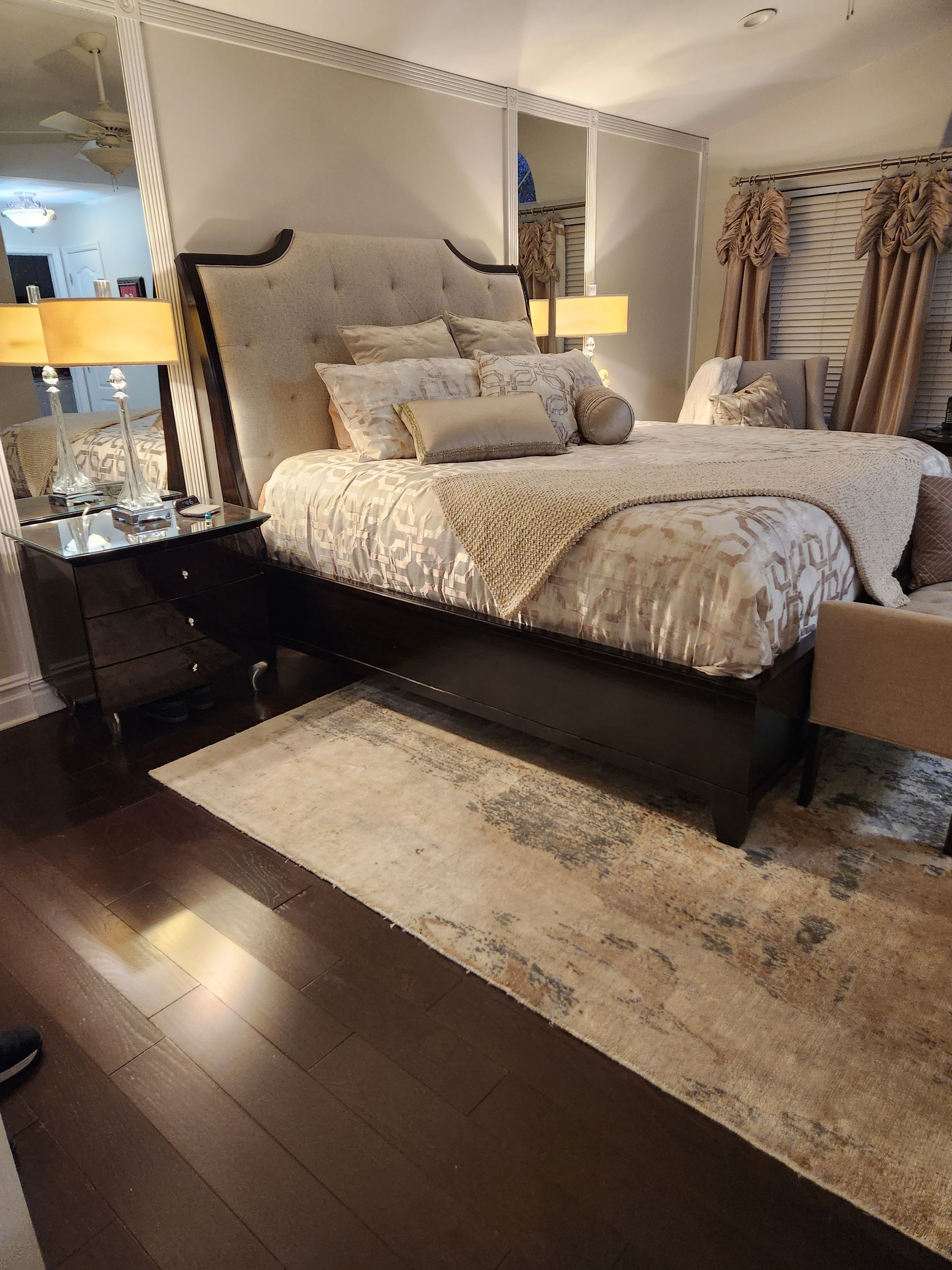 Bedroom with large bed, nightstands, rug, and window with curtains; dark wood floors.