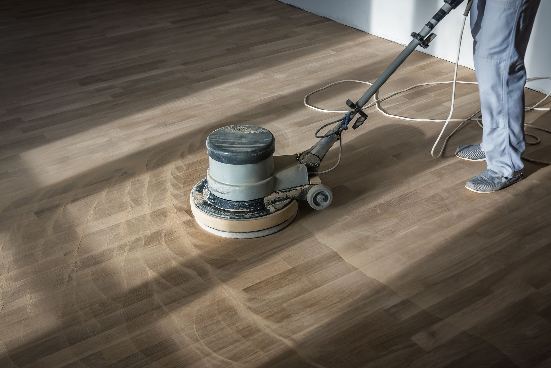 Person using a floor sander on a hardwood floor, creating wood dust.