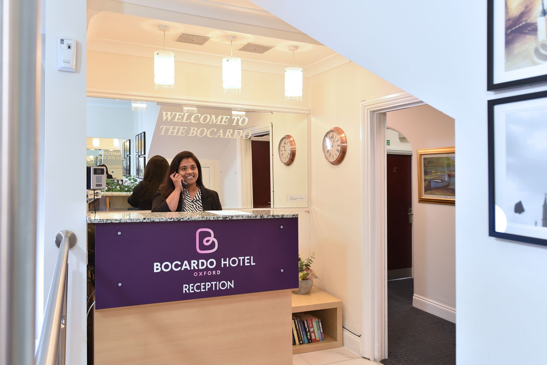 Receptionist talking on the phone at the Bocardo Hotel reception desk, located in a brightly lit, modern hotel lobby.