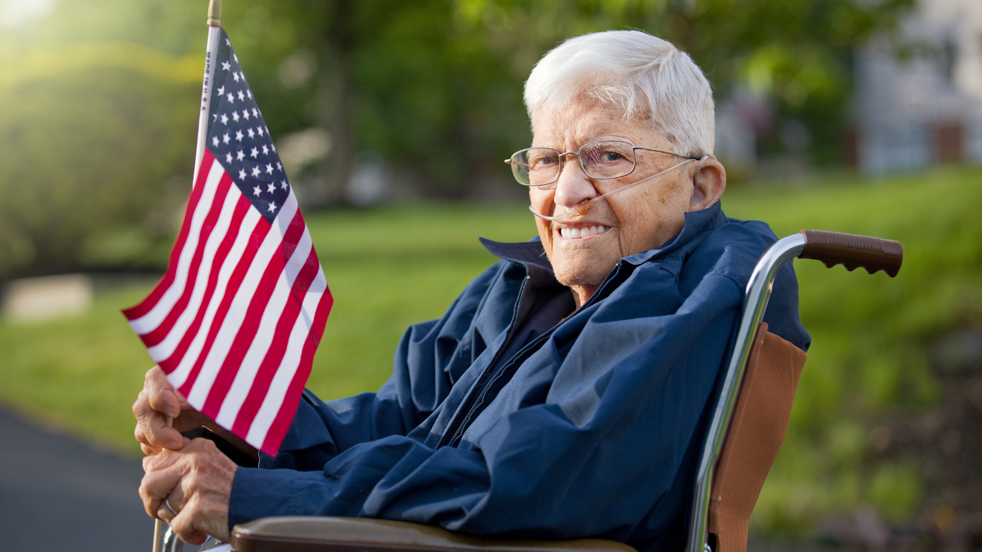 Elderly person in wheelchair holding small American flag.